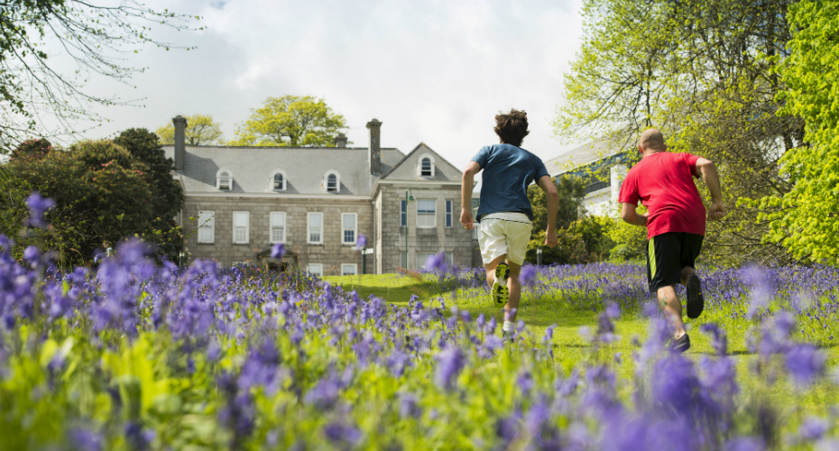 Two students running between the bluebells outside tremough house.