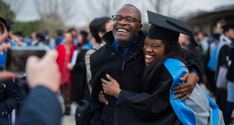 Black female graduate hugging and laughing with older black male.