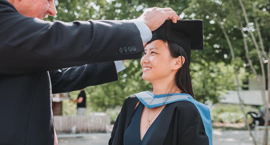 Man in suit adjusting a female graduand's mortorboard