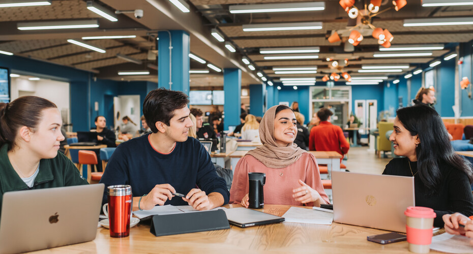 Four students with laptops sitting and talking in a cafe