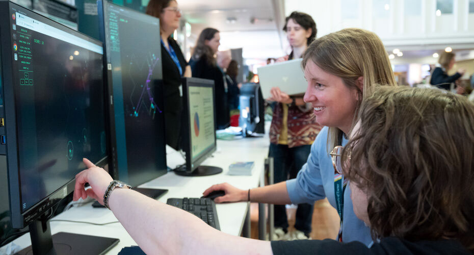Two people crouching down and looking at data on a PC screen.