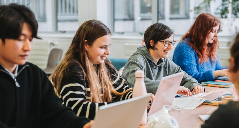 Students studying at a desk with notepads and laptops