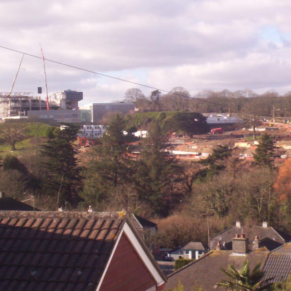 Fields and trees sloping upwards with rooftops at the bottom