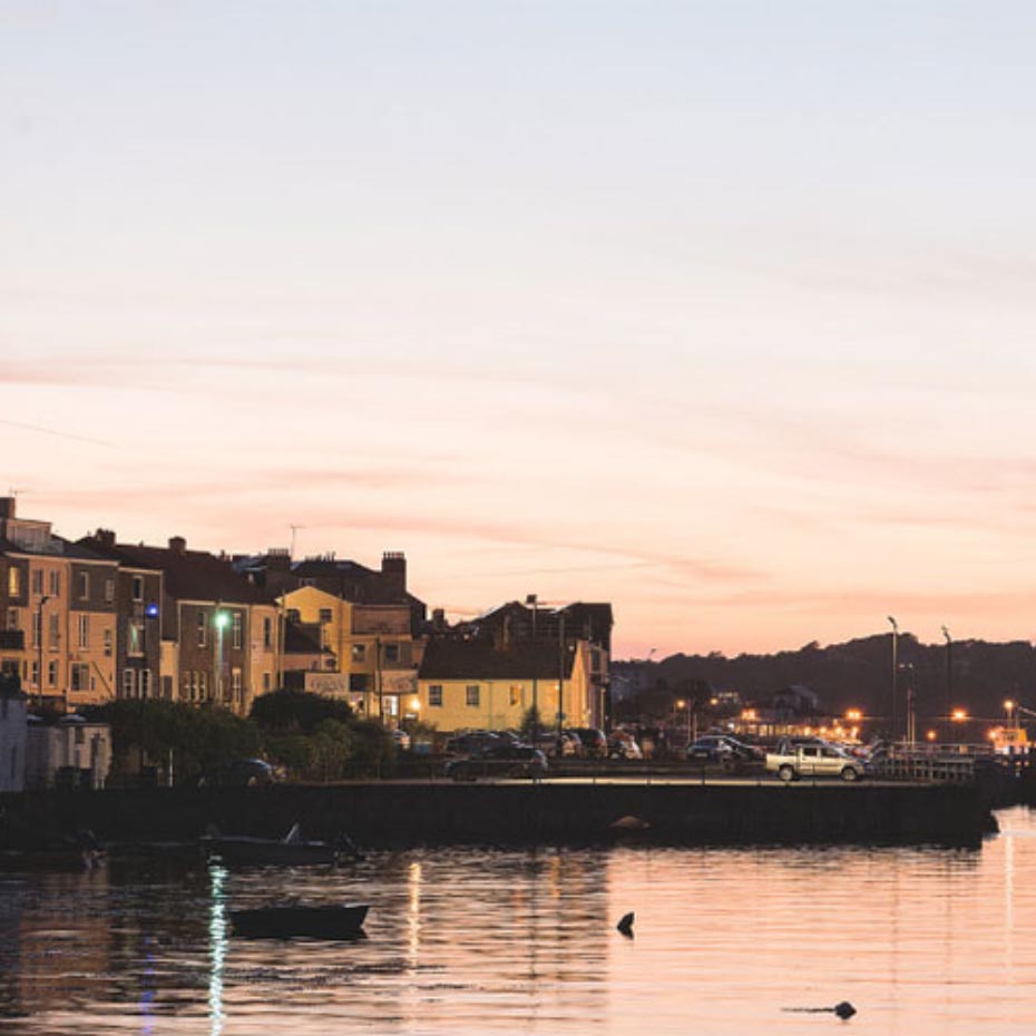 Water in front of buildings with sun setting in background