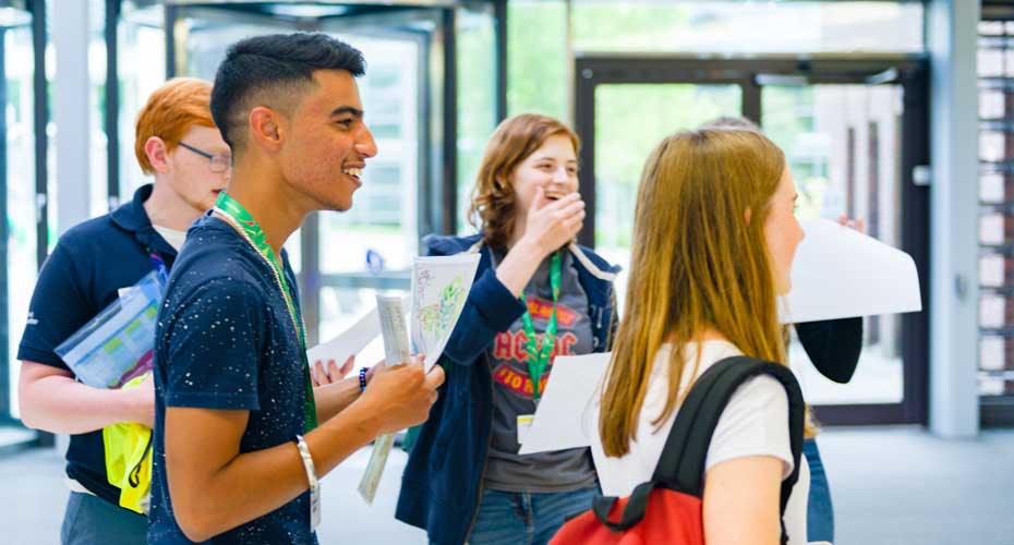 A group of students holding papers and wearing lanyards laughing