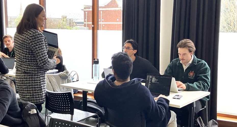 Student Michael Keegan sat with other Law Clinic students around a table with their laptops. One of the Clinic supervisors is stood talking to them.