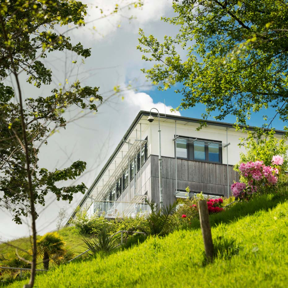 White brick building at the top of grass slope with trees either side