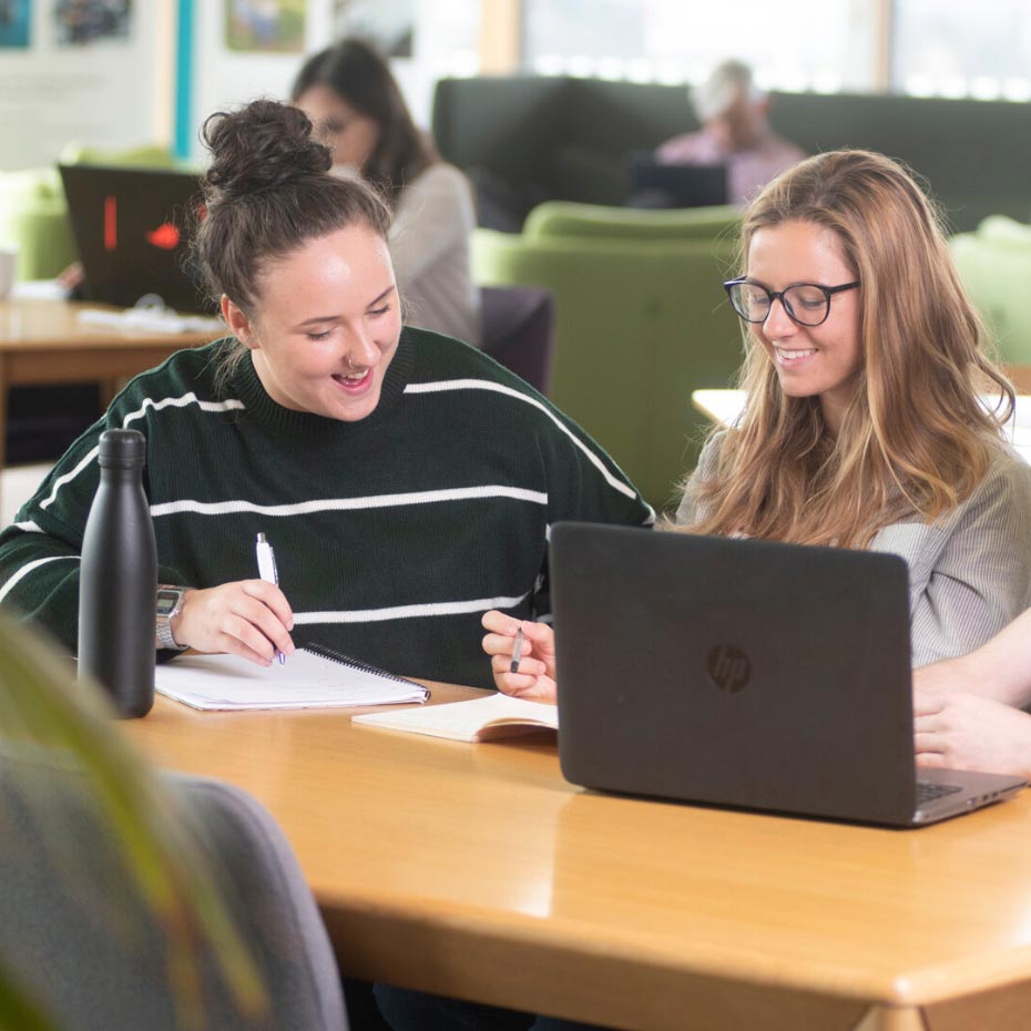 Two students sat at yellow table in front of a laptop