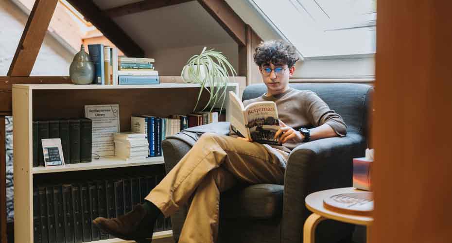 White male student sat in armchair reading in a bright and airy loft conversation space