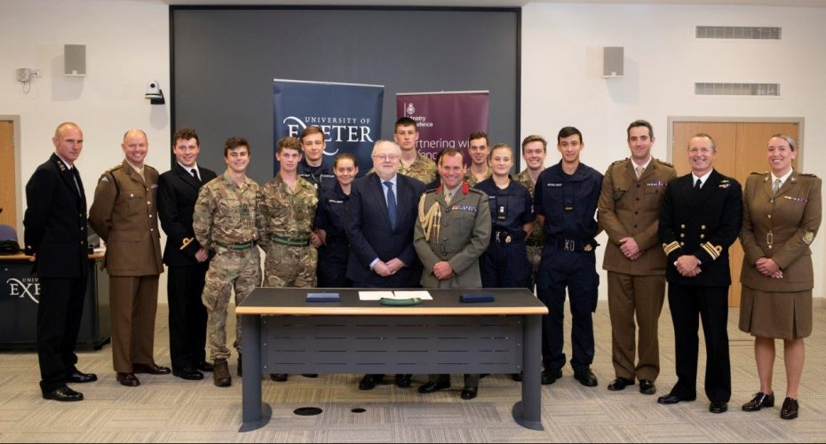 A diverse assembly of military personnel and university staff stands confidently before a table, showcasing the Armed Forces Covenant.