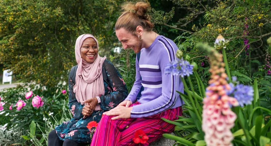 Two students laughing together in the gardens on Streatham Campus