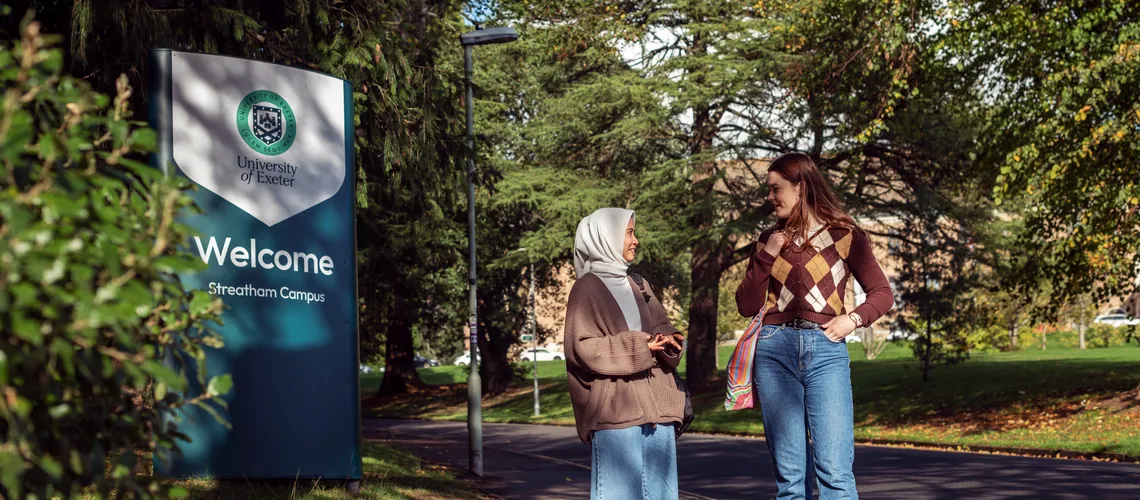 Students talking by the welcome sign on Streatham Campus in Autumn.