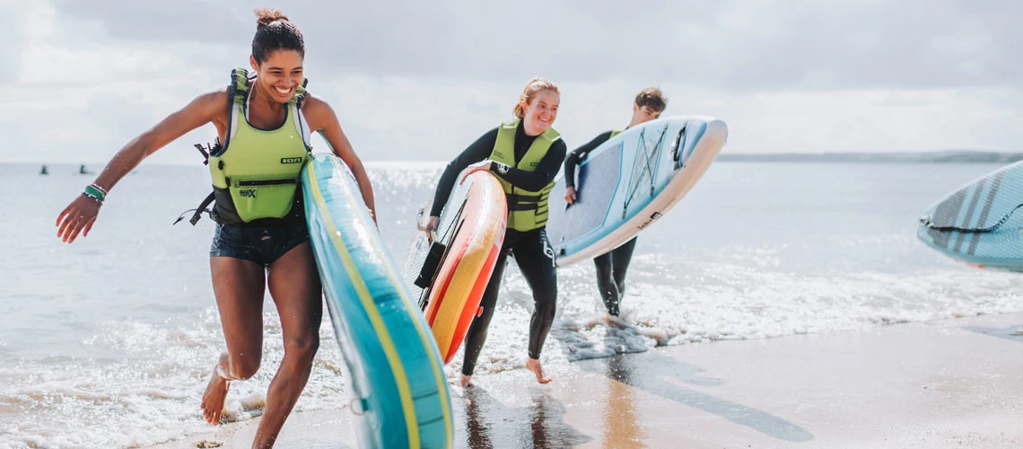 Students running out the sea with surfboards