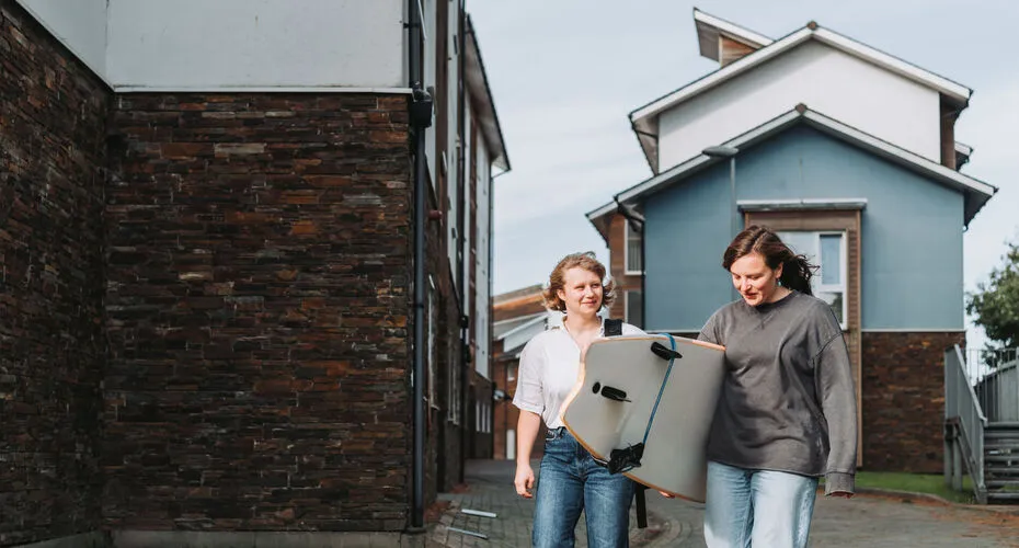 Students walking near their halls of residence with a surfboard
