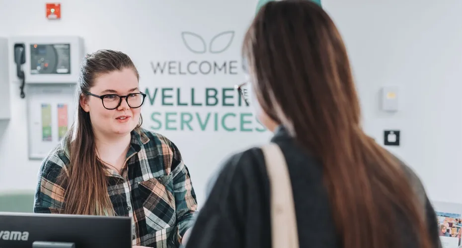 A student talking to a member of staff at the Wellbeing Services reception.