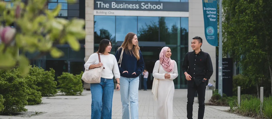 A group of students walking together outside of the Business School on Streatham Campus.