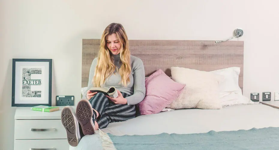 A student sitting on her double bed in the East Park halls of residence, Streatham Campus