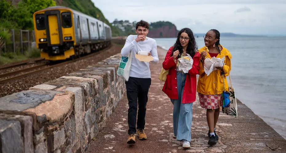 Students walking the sea wall at Teignmouth and eating fish and chips