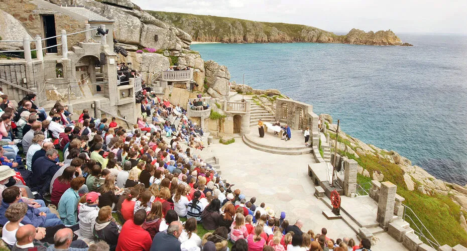 A crowd watching a performance at the open-air Minack Theatre set into the cliffside