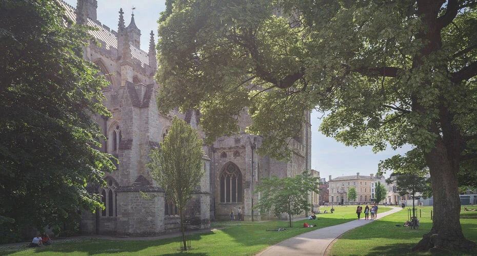 Exeter cathedral stands majestically with a lush green lawn and trees surrounding its impressive structure.