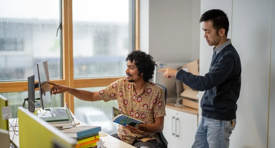 Two people collaborating on a computer in a modern office setting, focused on their work.