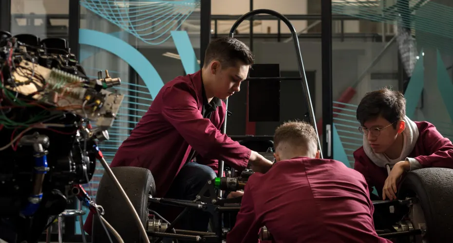 Three students engaged in engineering demonstrating teamwork and mechanical skills.