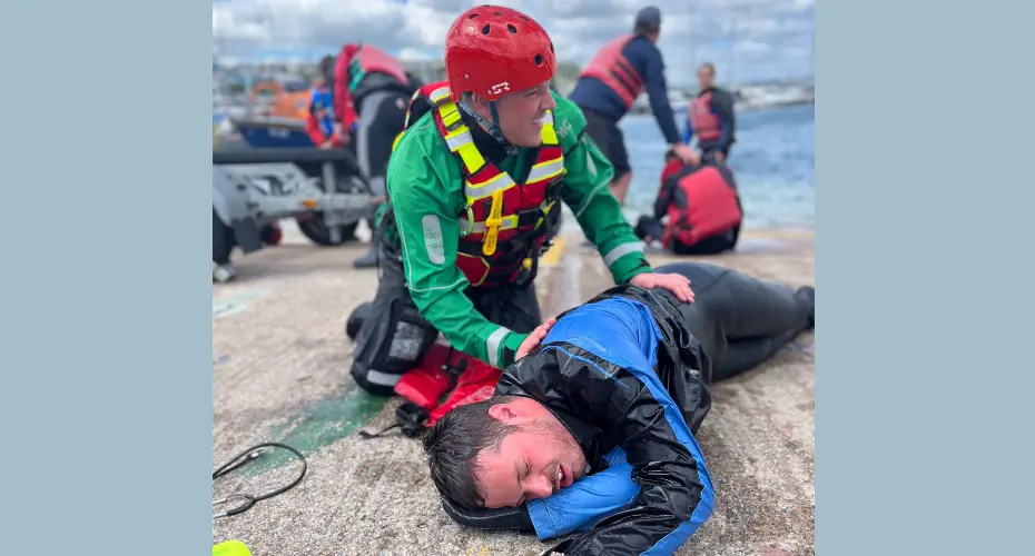 Extreme Medicine students on an ocean medicine residential in the UK. Demo patient lying on concrete near the shoreline with an Extreme Medicine student treating them