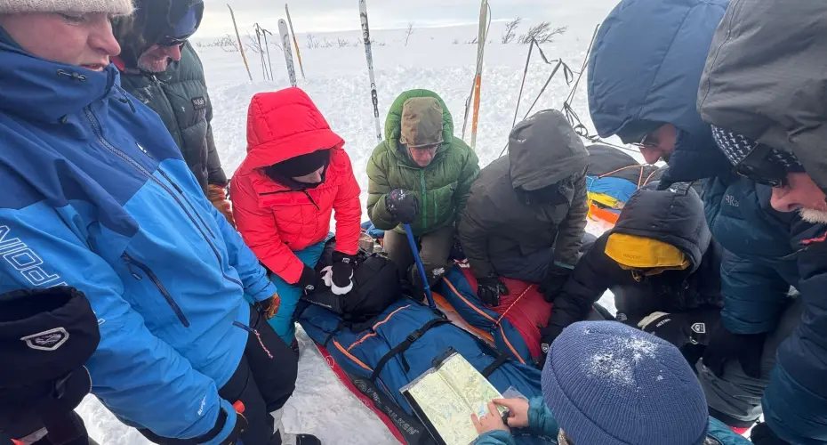 Extreme Medicine students in cold snowy environment, gathered around a patient and looking at a map together