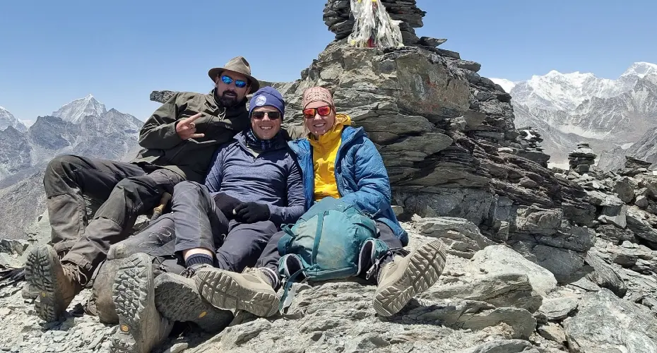 Two Extreme Medicine students with the expedition leader, sitting together on the rocks in a snowy cold mountain environment
