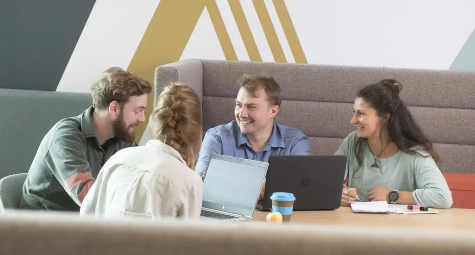 A group of mature students chatting and studying together with laptops